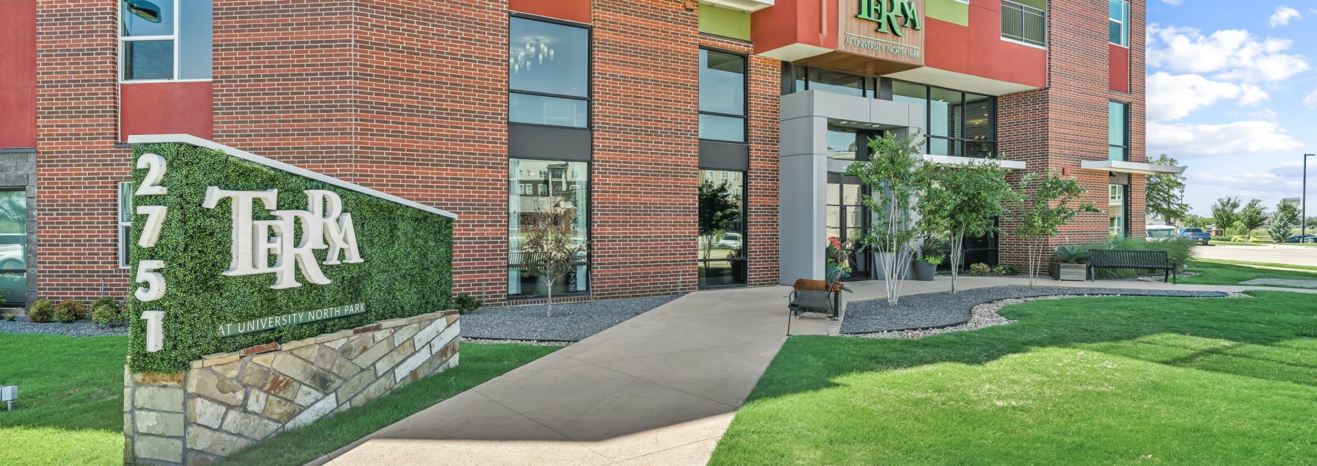 the front entrance to the apartment complex with a green lawn at The Terra at University North Park