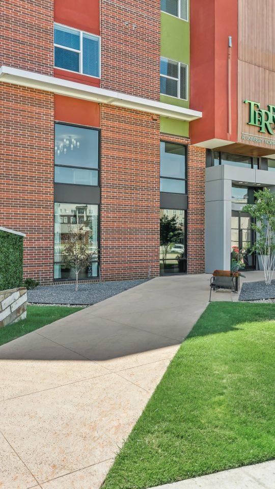 the front entrance to the apartment complex with a green lawn at The Terra at University North Park